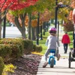 Pedestrians and a child riding a bicycle along a tree-lined sidewalk in Carmel, Indiana