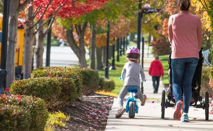 Pedestrians and a child riding a bicycle along a tree-lined sidewalk in Carmel, Indiana